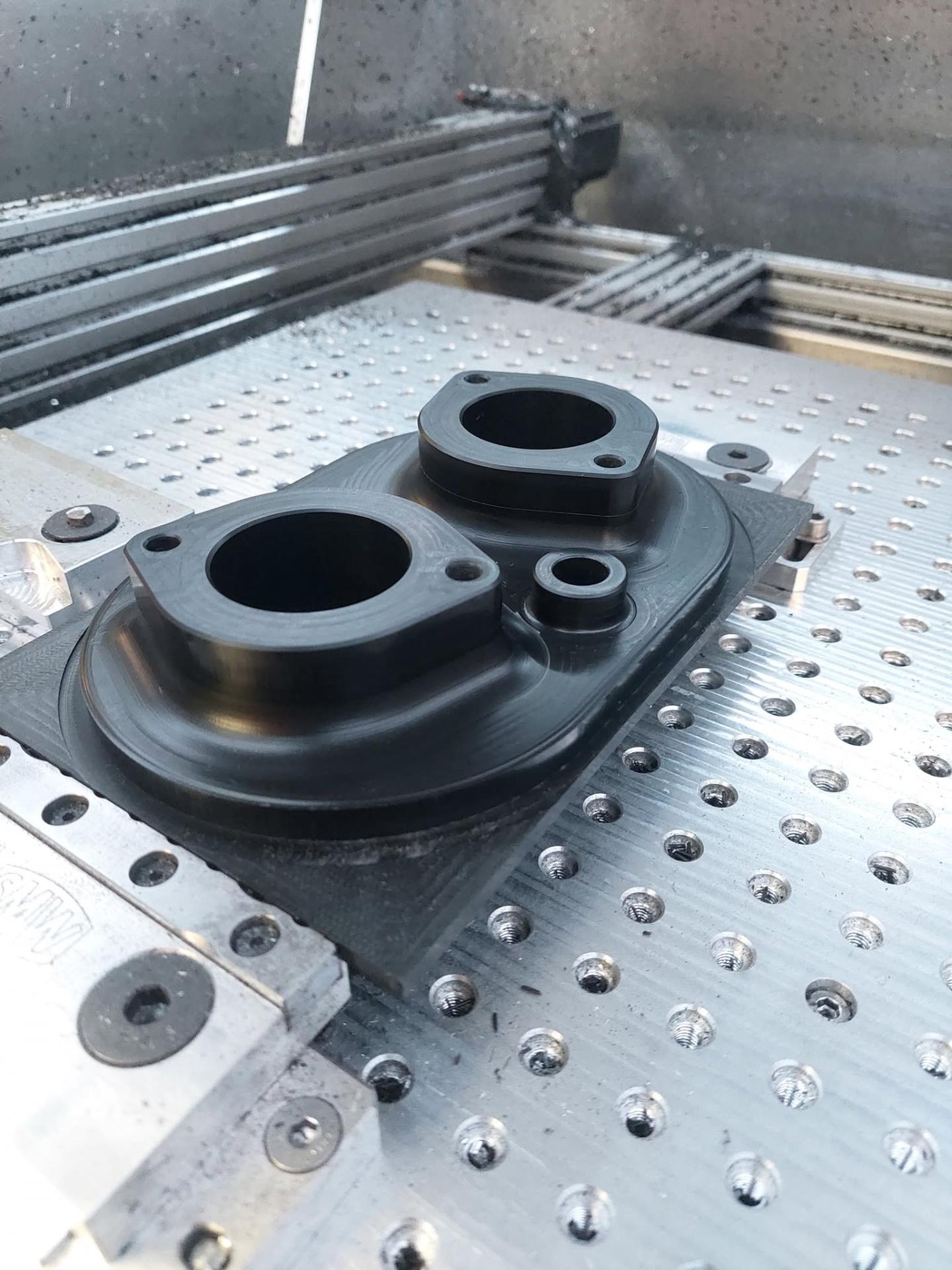 Machined black housing seated on a custom 3D-printed flip fixture on a CNC bed for OP2